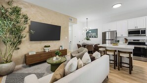 A modern living room with a sofa, a coffee table, a TV, and a dining area with chairs and a table. - 3BR Modern Home 15 Min to NRG, Downtown & Hobby (Houston)