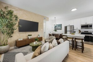 A modern living room with a sofa, a coffee table, a TV, and a dining area with chairs and a table. - 3BR Modern Home 15 Min to NRG, Downtown & Hobby (Houston)