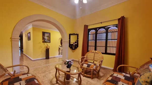 A room with yellow walls, a glass coffee table, wicker chairs, and a view through a barred window. - Casa Balfré - Traditional Home in Mérida (Mérida)