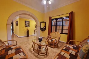 A room with yellow walls, a glass coffee table, wicker chairs, and a view through a barred window. - Casa Balfré - Traditional House in Mérida   (Mérida)
