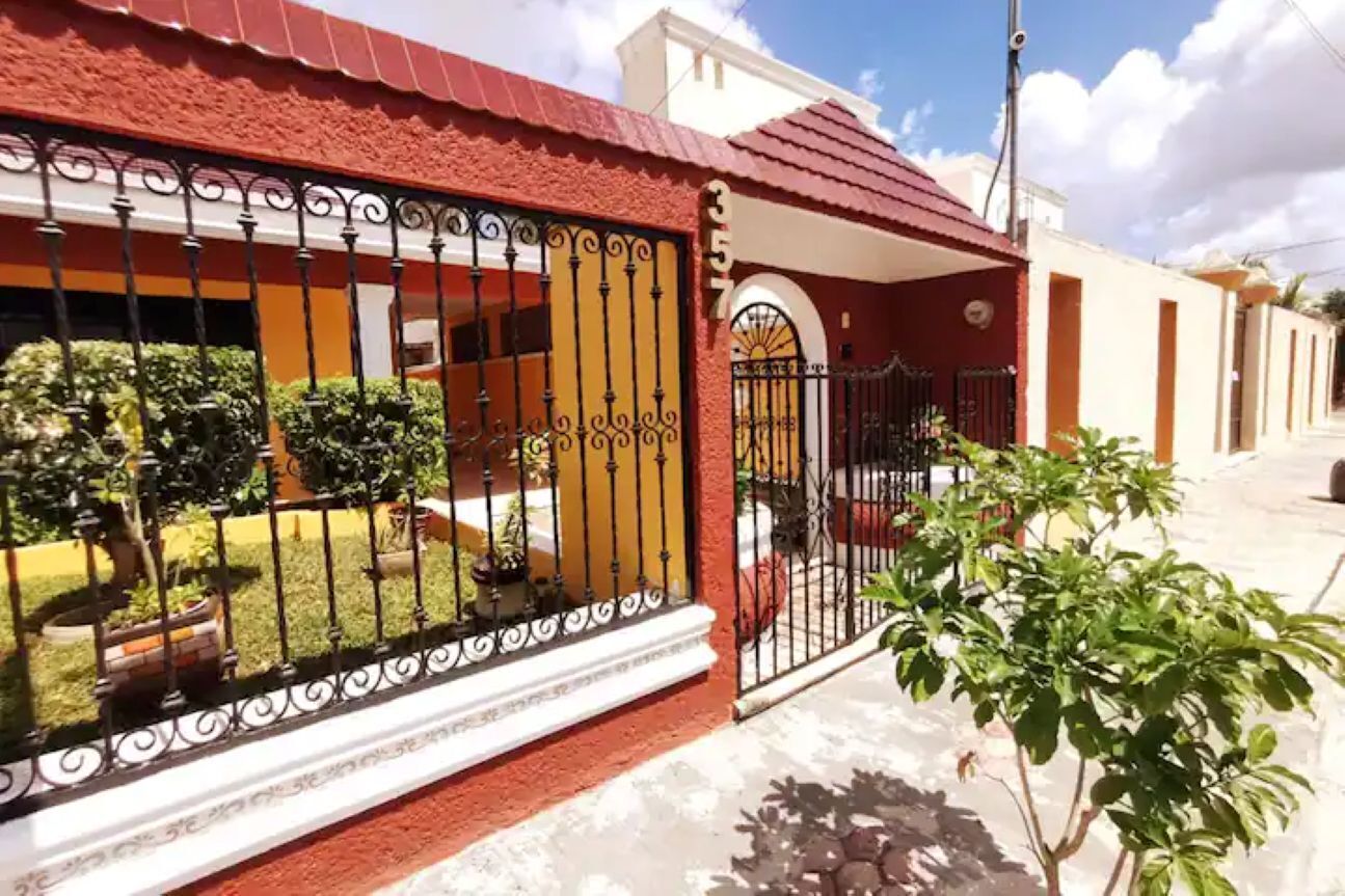 Una casa con techo rojo, entrada protegida por una reja y un pequeño jardín.