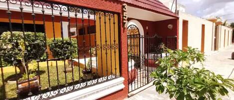 Una casa con techo rojo, entrada protegida por una reja y un pequeño jardín.
