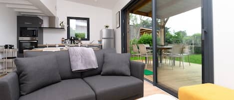 A modern living room with a grey sofa, a yellow ottoman, and a sliding glass door leading to an outdoor patio.