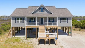 A two-story beach house with a front porch, wooden deck, and a view of the beach. - Turtle LIVIN | ICW Views, Sleeps 11, Games & Relax (North Topsail Beach)