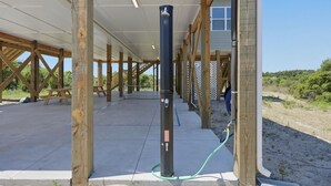 A covered outdoor area with wooden beams, a concrete floor, and a black pole with a hose. - Turtle LIVIN | ICW Views, Sleeps 11, Games & Relax (North Topsail Beach)