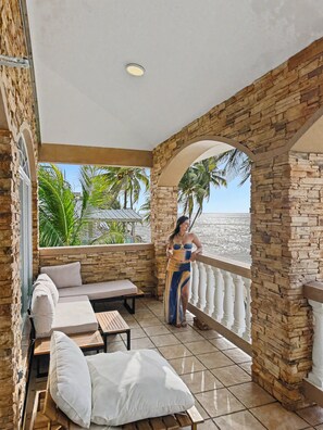 A balcony with stone walls, a cushioned seating area, and a view of the sea. - Oceanfront 2-Story Villa with Hot Tub, 180° Ocean Views, and Sunsets – Sleeps 8 (Aguada)