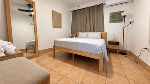 A bedroom with a wooden bed, a bedside table, a lamp, and a mirror. - 2-story villa with ocean views, hot tub, 180° ocean views, and sunsets – sleeps 8   (Aguada)