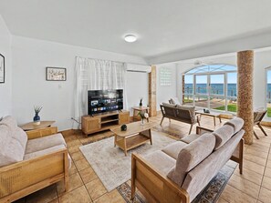 A living room with a television, seating, and a view of the sea. - 2-story villa with ocean views, hot tub, 180° ocean views, and sunsets – sleeps 8   (Aguada)