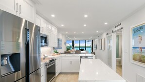 A modern kitchen with stainless steel appliances, white cabinetry, and a large window overlooking a body of water. - Luxury Waterfront 2BR/2BA Marco Island condo (Marco Island)