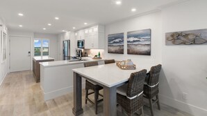 A modern kitchen with white cabinets, a central island, and a dining area with wicker chairs. - Luxury Waterfront 2BR/2BA Marco Island condo (Marco Island)