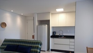 Uma cozinha compacta com armários brancos, geladeira embutida e bancada preta.
