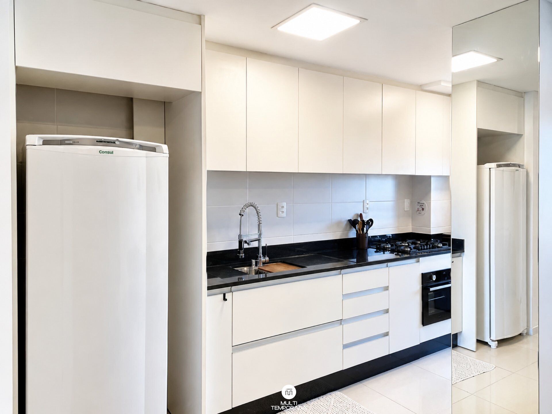 A modern kitchen with white cabinetry, a black countertop, a stainless steel sink, a gas stove, and a built-in oven.