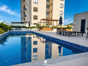 Une piscine aux carreaux bleus, entourée d’un espace extérieur aménagé avec des sièges et d’un bâtiment à plusieurs étages.