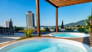 Un espace piscine sur le toit, comprenant deux bains à remous, une terrasse en bois et une vue sur le paysage urbain.