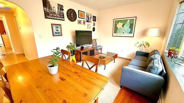 A living room with a wooden dining table, a blue sofa, a TV, and various wall art.