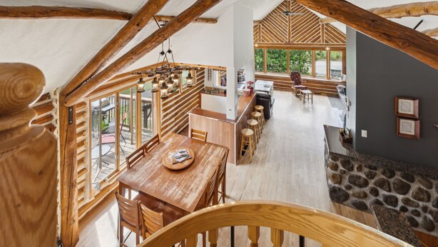 A spacious loft-style room with a high ceiling, wooden beams, a dining area with a wooden table and chairs, and a stone fireplace. - 🌲Chalet Spa & Sauna Getaway in Luarentide– Sainte-Lucie 🌲 Val-David, Val-Morin (Sainte-Lucie-des-Laurentides)