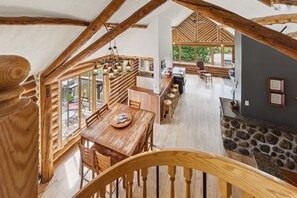 Una habitació d'estil loft espaiosa amb un sostre alt, bigues de fusta, una zona de menjador amb taula i cadires de fusta, i una llar de pedra.