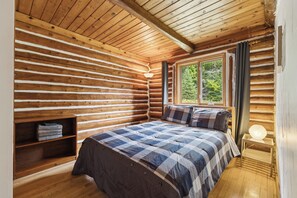 Een slaapkamer in een blokhut met een bed, een plank, een raam en een lamp.