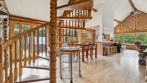 A spacious loft-style interior with a wooden staircase, a dining area, and large windows offering views of the outdoors. - 🌲Chalet Spa & Sauna Getaway in Luarentide– Sainte-Lucie 🌲 Val-David, Val-Morin (Sainte-Lucie-des-Laurentides)