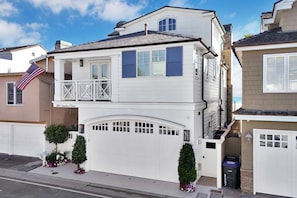 A two-story house with a white exterior, a garage, and a small balcony. - Luxury Newport Beach House with Rooftop Sunset Deck, Hot Tub and Game Room (Newport Beach)