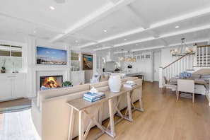 A spacious living area with a fireplace, a large painting, and a dining area with a staircase. - Luxury Newport Beach House with Rooftop Sunset Deck, Hot Tub and Game Room (Newport Beach)
