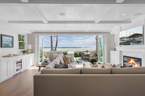 A spacious living room with a large sofa, a fireplace, and a view of the beach. - Luxury Newport Beach House with Rooftop Sunset Deck, Hot Tub and Game Room (Newport Beach)