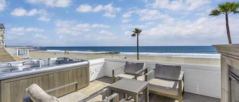 A patio with outdoor seating, a hot tub, and a view of the beach.