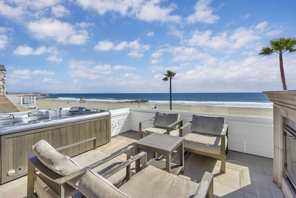 A patio with outdoor seating, a hot tub, and a view of the beach.