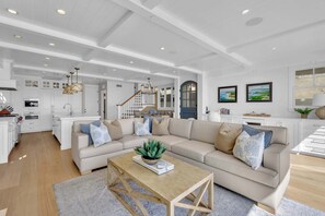 A spacious living area with a large beige sofa, a wooden coffee table, and a staircase leading to an upper level. - Luxury Newport Beach House with Rooftop Sunset Deck, Hot Tub and Game Room (Newport Beach)