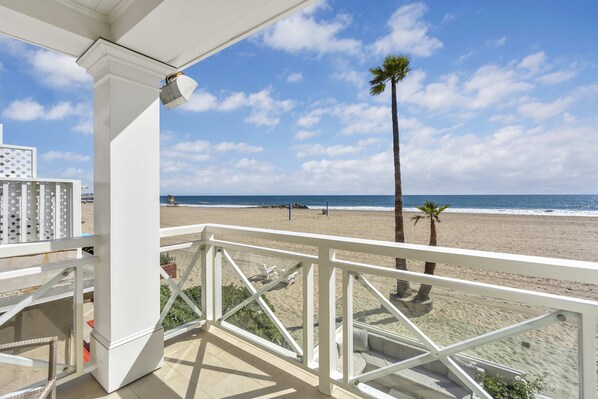 A balcony with a view of the beach, palm trees, and a clear sky.
