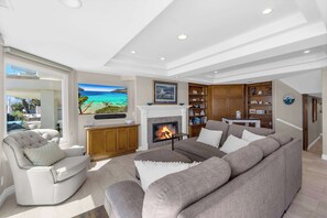 A living room with a fireplace, a large TV, and a view of the ocean. - 4207 Seashore Beachfront Oasis Rooftop and Firepit, Sleep 12 (Newport Beach)