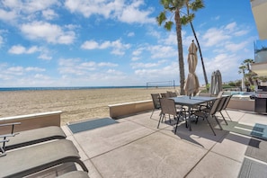 A beachside patio with a table and chairs, palm trees, and a view of the ocean. - 4207 Seashore Beachfront Oasis Rooftop and Firepit, Sleep 12 (Newport Beach)