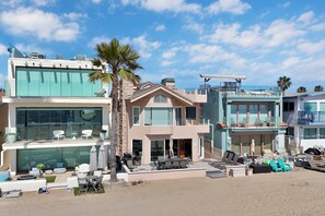A modern beachfront property with a large patio, outdoor seating, and a palm tree. - Beachfront Oasis: Rooftop and Firepit, Sleep 12 (Newport Beach)