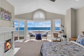 A bedroom with a large bed, a fireplace, a view of the beach, and a seating area with chairs. - 4207 Seashore Beachfront Oasis Rooftop and Firepit, Sleep 12 (Newport Beach)