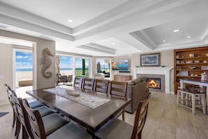 A spacious dining area with a large table and chairs, a fireplace, and a view of the outdoors. - 4207 Seashore Beachfront Oasis Rooftop and Firepit, Sleep 12 (Newport Beach)