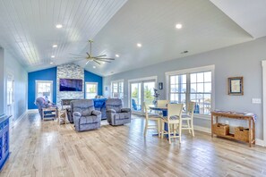 A spacious living room with a stone fireplace, a ceiling fan, and a dining area with a table and chairs. - "The Haven of Rest" – Multi-Gen Luxury Beach House w/ Elevator & Rooftop Views! (Milton)