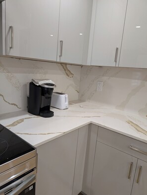 Een keuken met witte kastjes, een koffiezetapparaat, een broodrooster en een magnetron.