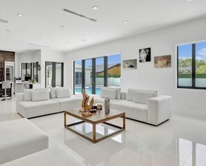 A modern living room with a white sofa set, a wooden coffee table, and large windows offering a view of a swimming pool. - Palm paradise (Miami)