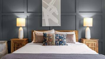 A bed with a headboard, two bedside tables with lamps, a patterned throw blanket, and a wall with a geometric painting.