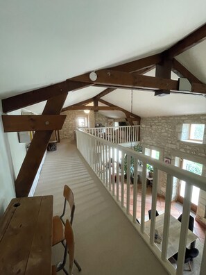 A spacious loft with a high ceiling, exposed wooden beams, a balcony with a white railing, and a stone wall. - Beautiful country house 3 km from Angoulême (Soyaux)