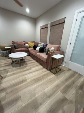 A living room with a sectional sofa, a round coffee table, and a small side table. - Cozy Anime Beach House - Quick Walk to Beach (Bolivar Peninsula)