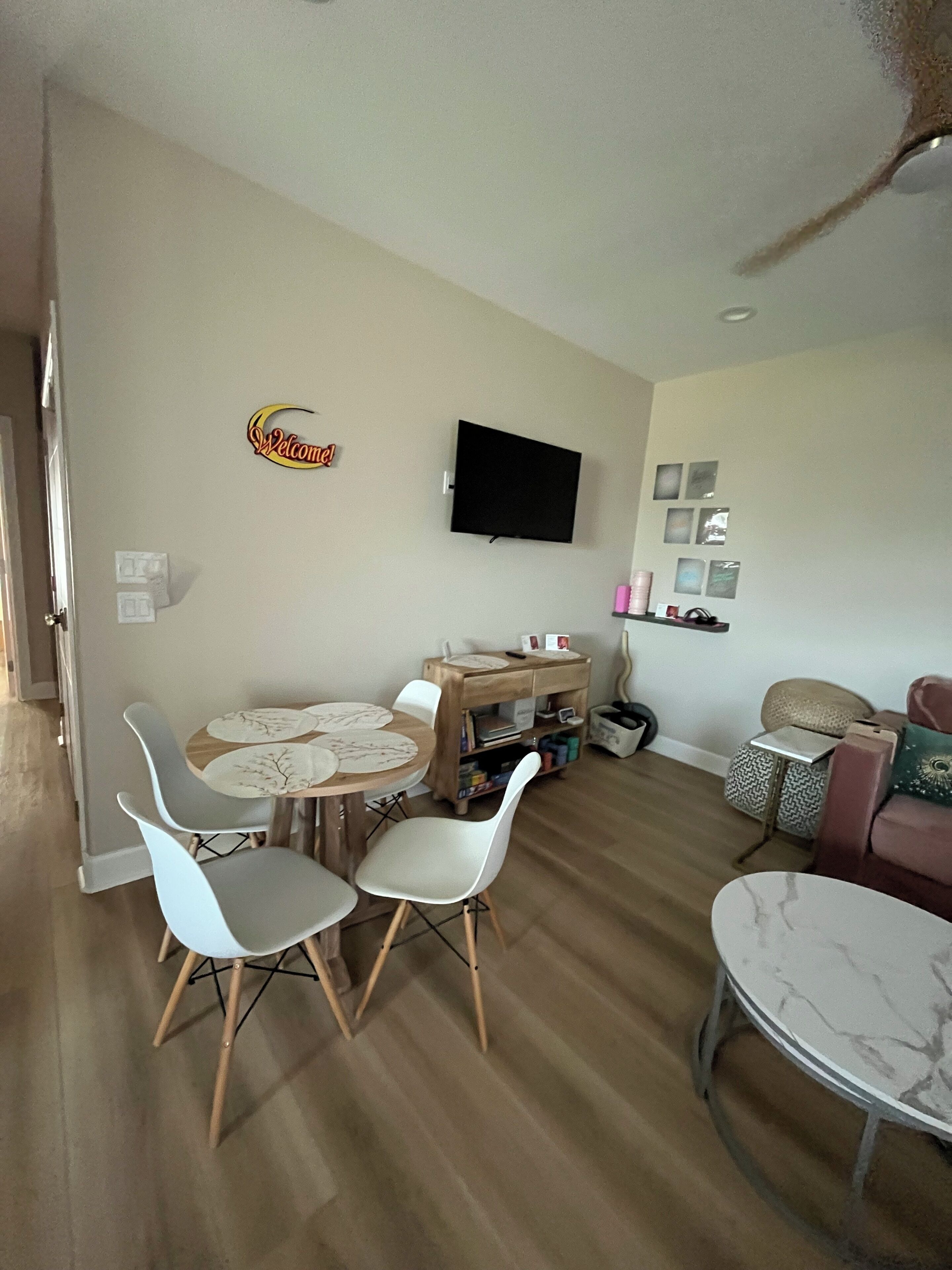 Uma sala de estar com área de jantar, uma televisão de tela plana na parede e uma pequena mesa lateral com luminária.