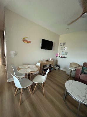 Ein Wohnzimmer mit Essbereich, einem an der Wand befestigten Flachbildfernseher und einem kleinen Beistelltisch mit Lampe.