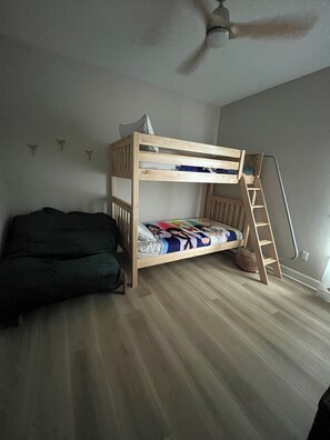 Een stapelbed met een ladder, een slaapbank en een plafondventilator in een kamer met houten vloeren.