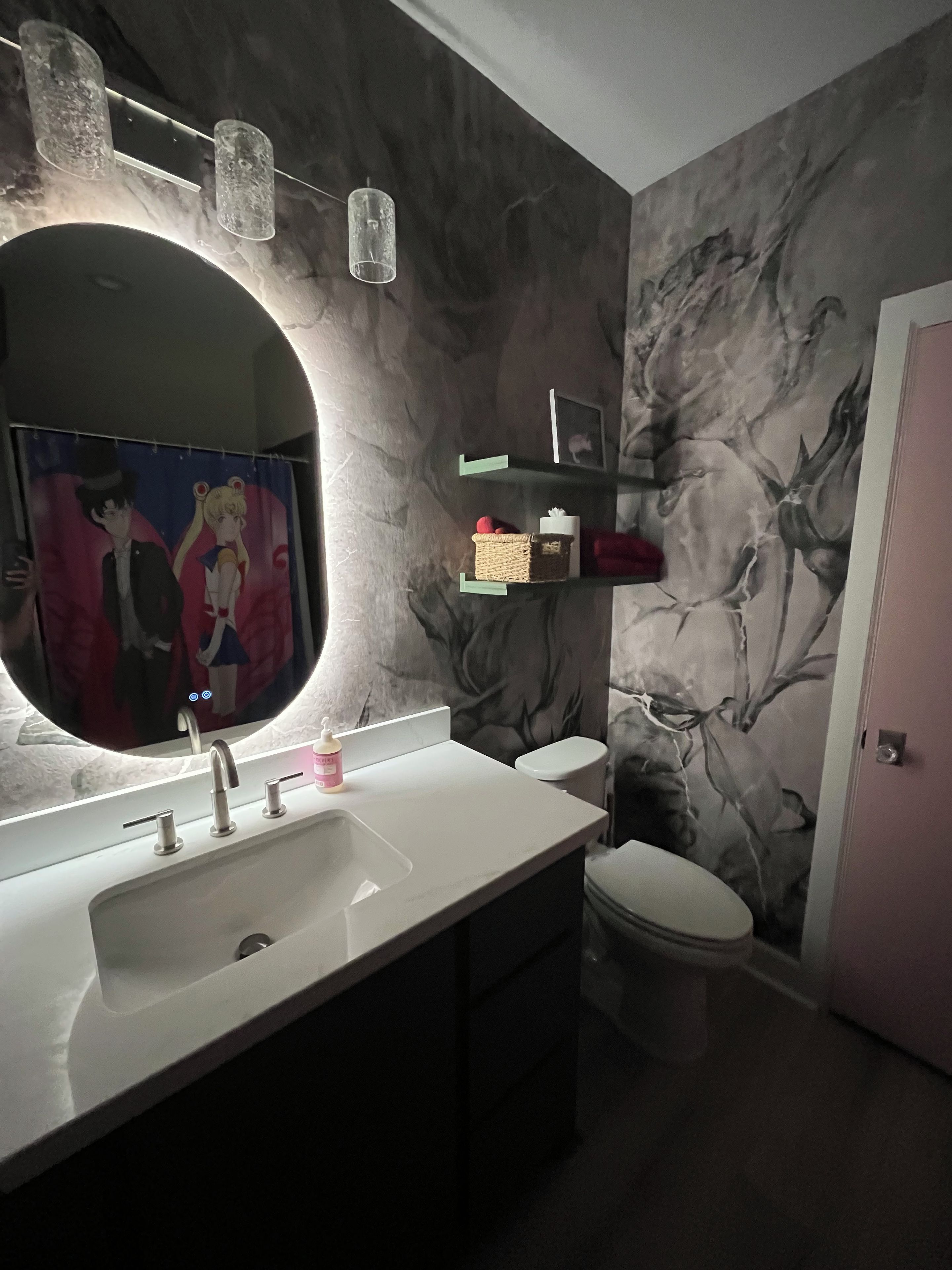 Ein Badezimmer mit einem großen Spiegel, einem Waschbecken mit mehreren Wasserhähnen, einer Toilette und einer Wand mit floralem Wandbild.