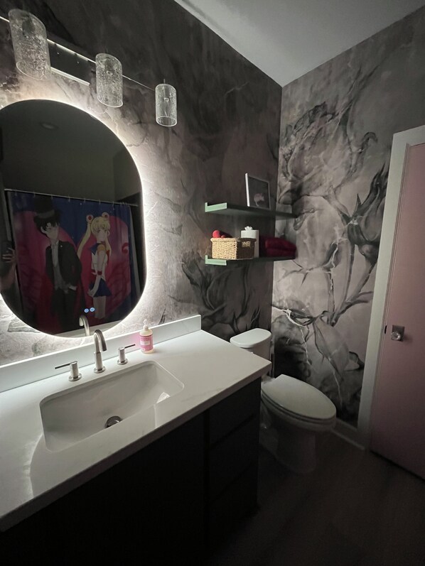Un bagno con uno specchio grande, un lavabo con diversi rubinetti, un water e una parete con un murale floreale.