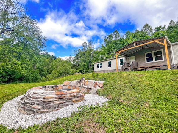 A house with a stone fire pit, a covered porch, and a grassy yard.