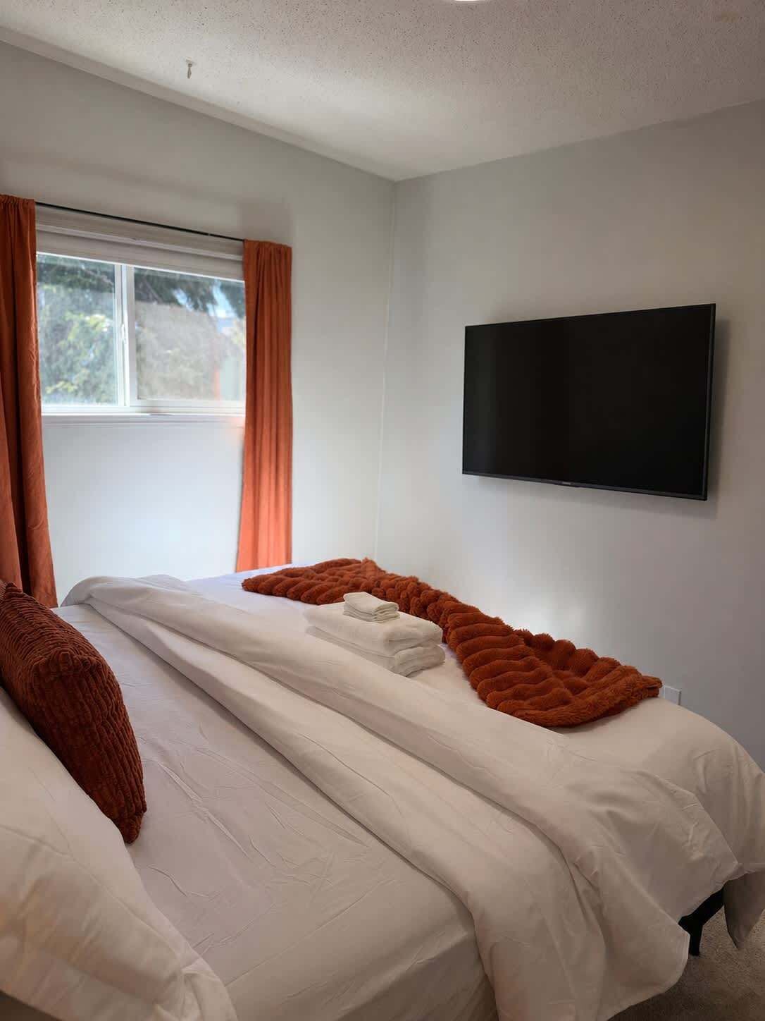 Ein Hotelzimmer mit zwei Betten, einem an der Wand befestigten Fernseher und einem Fenster mit Vorhängen.