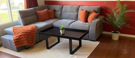 Ein Wohnzimmer mit einem Ecksofa, einem Couchtisch und einer Topfpflanze.