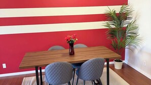 A dining area with a wooden table, two grey chairs, a vase with flowers, and a potted plant. - Cozy 2BR Near Zoo, Downtown & Max Bell (Calgary)